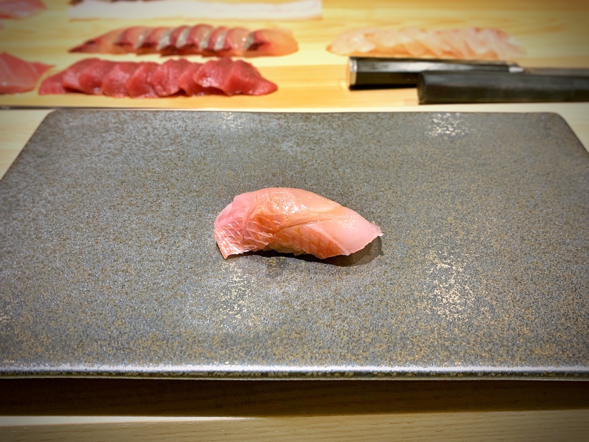 Un pequeño trozo de sushi rosa en un plato cuadrado gris.