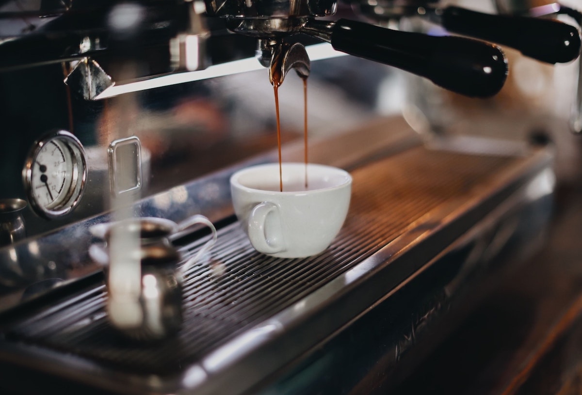 cerrar la máquina de espresso vertiendo espresso en una pequeña taza blanca