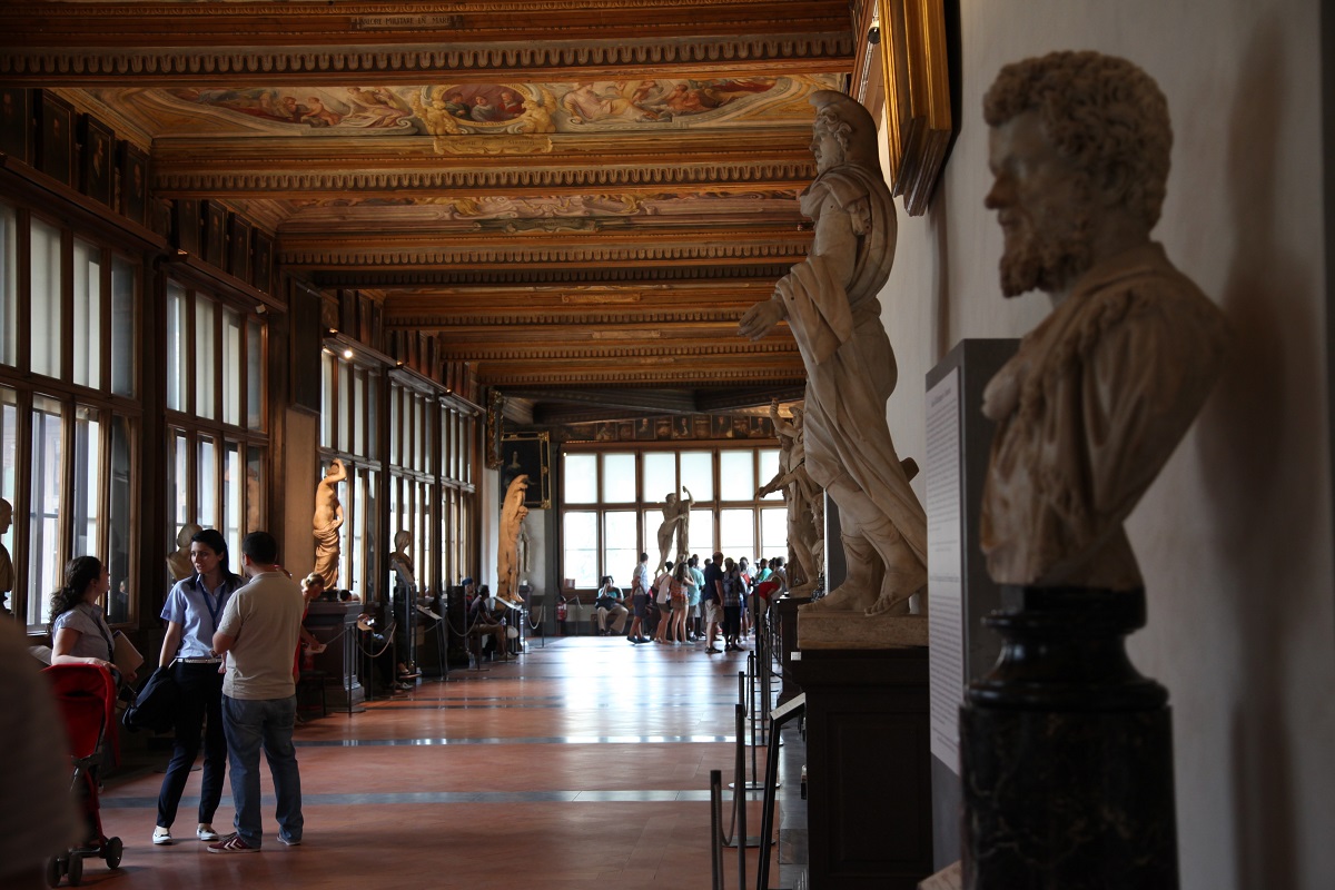 Un largo pasillo dentro de un museo de arte con estatuas y un techo dorado
