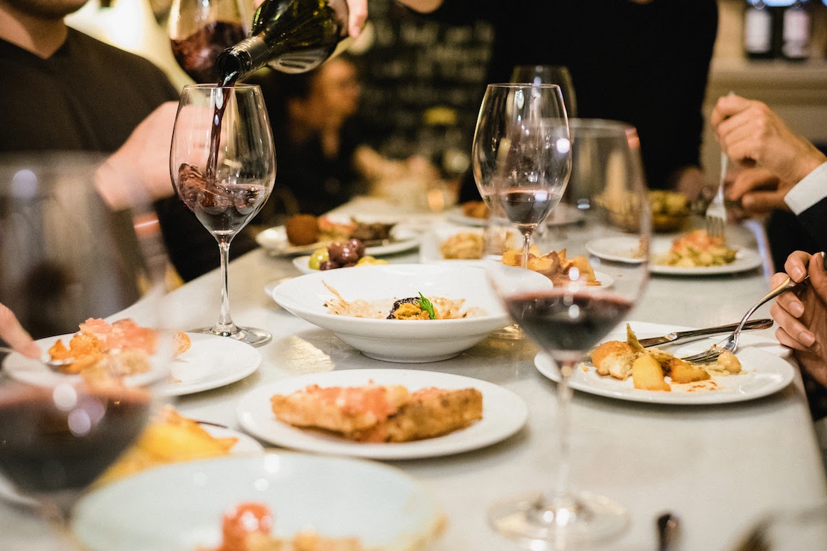 Una mesa llena de múltiples platos pequeños de tapas y copas de vino tinto.