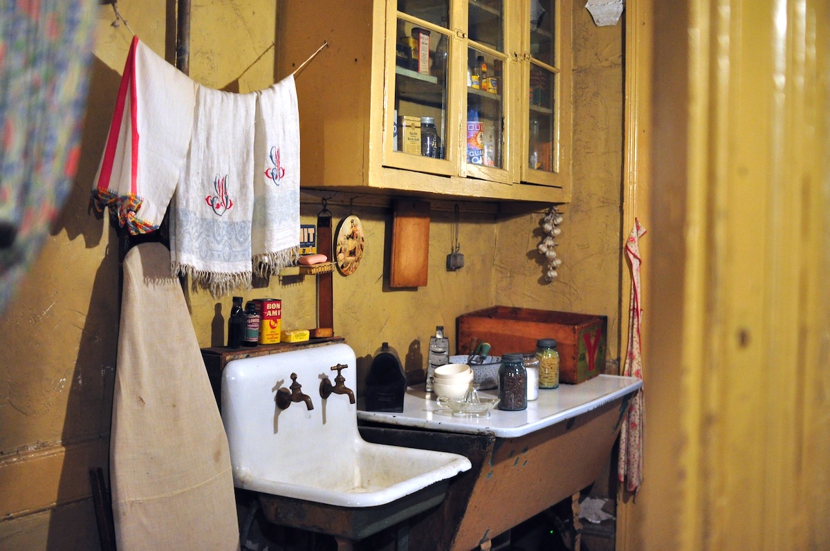 Una cocina antigua en un piso con toallas colgando sobre un fregadero pequeño