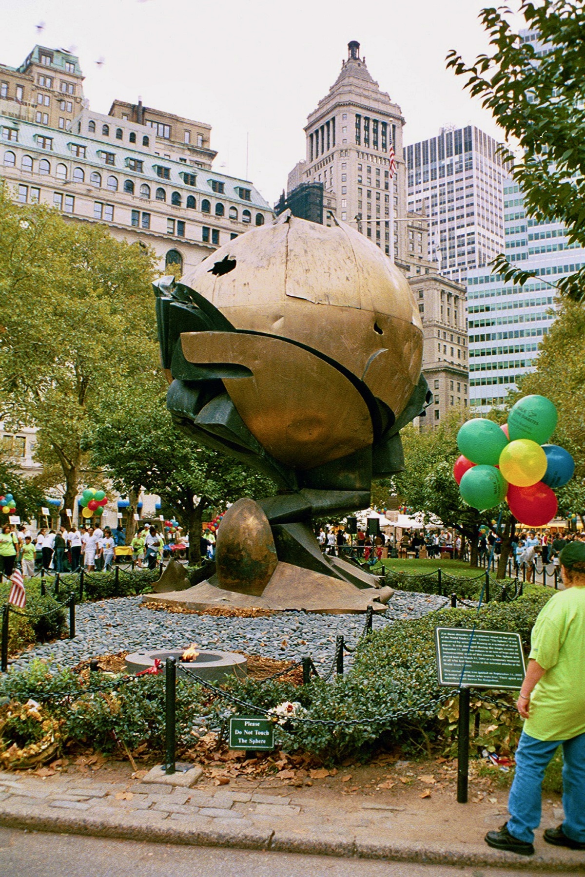 Una gran estatua de bronce circular en medio de un concurrido parque urbano