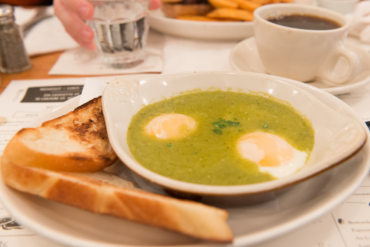 Huevos cocidos en salsa verde en un plato sobre un plato blanco junto a dos tostadas