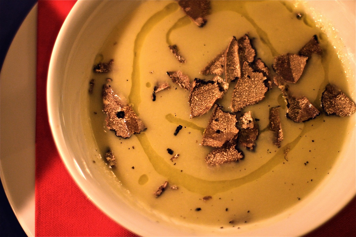 Un tazón blanco de sopa amarilla rociada con aceite de oliva y trufas afeitadas