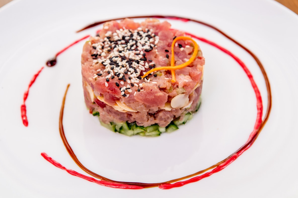 Tartar de atún rodeado de anillos de salsa roja en un plato blanco