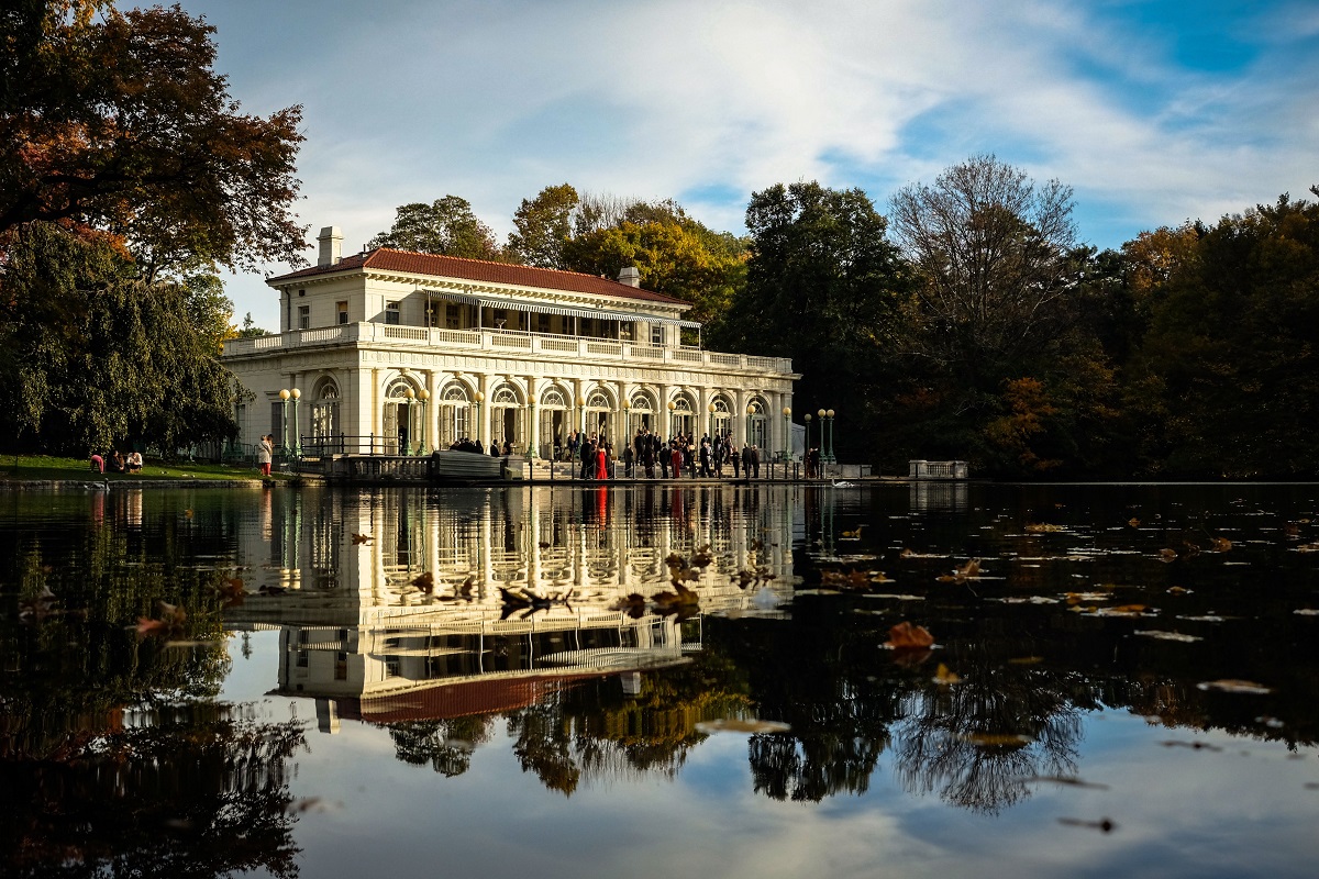 Un gran edificio antiguo adornado se encuentra en la orilla del agua rodeado de árboles en un parque
