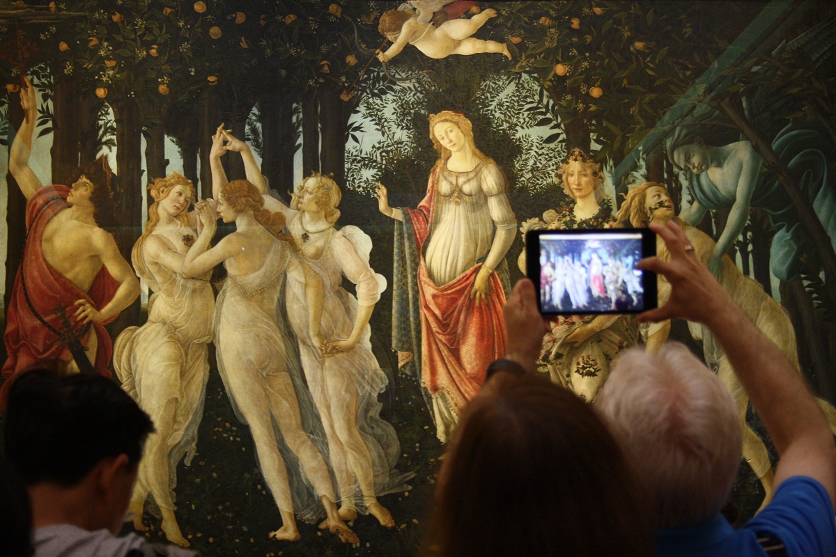 Visitantes en un museo de arte toman fotografías de una pintura de mujeres en un bosque