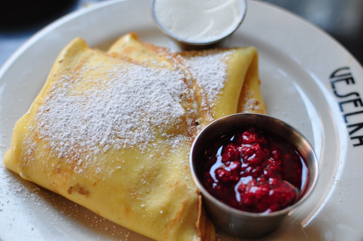Crepes espolvoreados con azúcar en polvo junto a un pequeño recipiente de frutos rojos rallados.