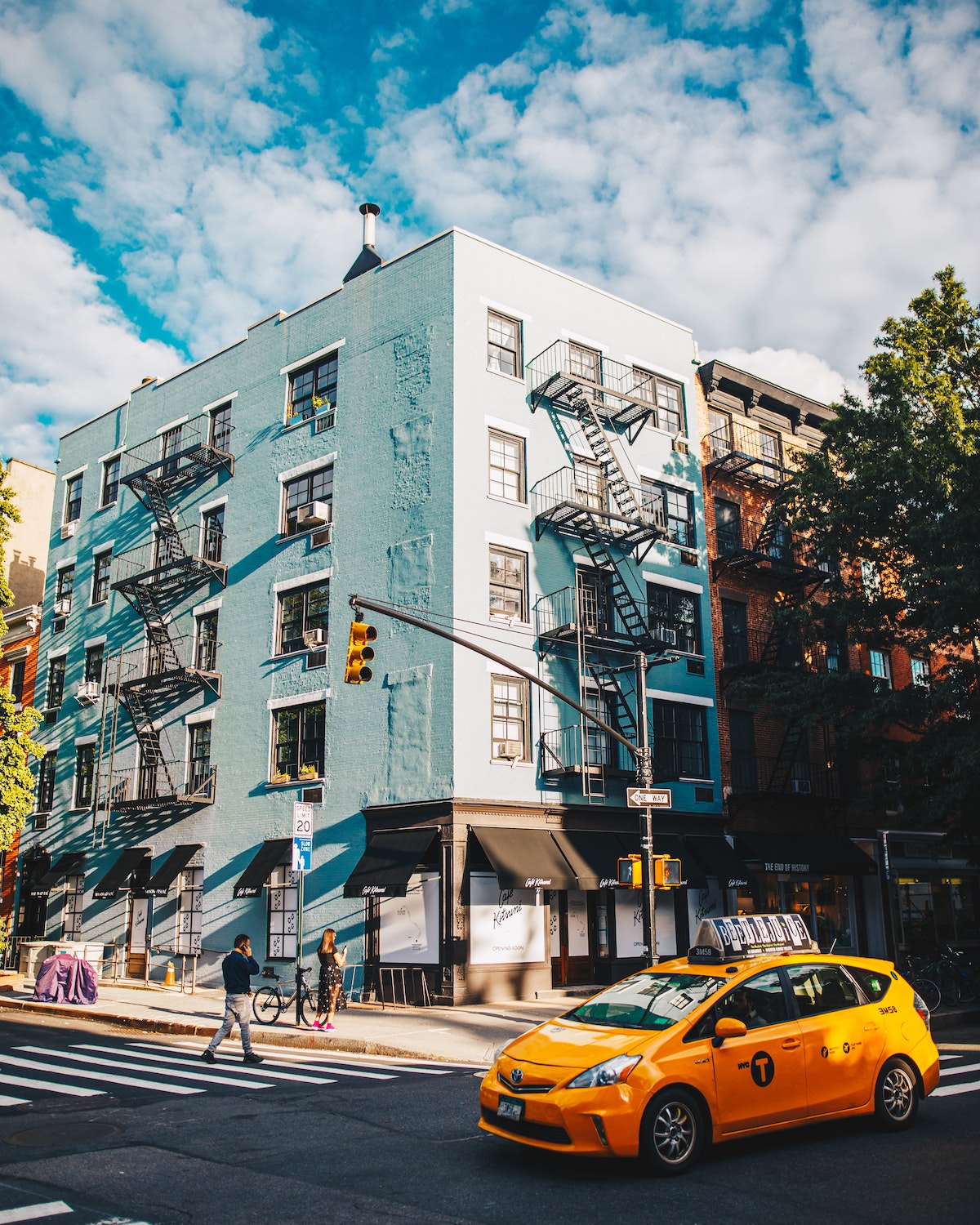Un edificio azul pálido en la esquina de una calle con un taxi amarillo conduciendo afuera.